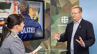 Eine Soldatin und ein Mann stehen sich vor einem Monitor gegenüber und sprechen miteinander
