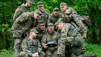 Soldaten blicken einem Kameraden über die Schulter, der eine Steuereinheit einer Drohne hält.