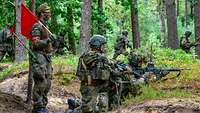 Zwei Soldaten beim Schießen, ein Sicherheitsgehilfe mit roter Fahne steht dahinter.