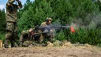 Ein Soldat beobachtet das Gelände mit einem Fernglas. Ein Soldat bedient das Maschinengewehr.
