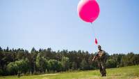 Ein Soldat lässt auf einem Truppenübungsplatz einen pinken Wetterballon steigen