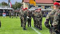 Soldaten stehen sich auf einer Rasenfläche in Formation gegenüber, ein Soldat hält eine Truppenfahne.