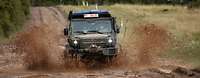 Ein Geländewagen Wolf 2 fährt im Gelände durch eine Pfütze und Schlamm spritzt hoch
