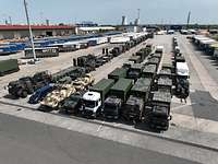 Several vehicles are parked in a large parking area at the port