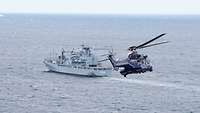 Ein Hubschrauber der Polizei im Anflug auf eine Marineschiff in See.