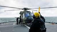 Auf einer Landefläche auf einem Schiff steht ein Hubschrauber der Bundeswehr, davor steht ein Soldat.