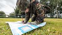 Ein Soldat in Flecktarnuniform beugt sich über eine Landkarte.