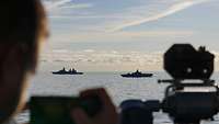 Zwei Kriegsschiffe in See fahren von rechts nach links.
