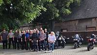 Menschen stehen neben Motorrädern vor einem alten Gebäude
