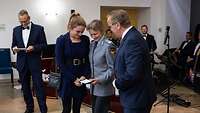 Boris Pistorius schaut mit einer Soldatin und ihrer Angehörigen auf die Medaille in ihrer Hand.