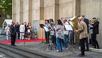 Ein Posaunenchor steht vor einem Kircheneingang und spielt Musik.