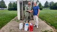 Ein Soldat und ein Zivilist stehen vor einem Glockenturm und reichen sich die Hände.