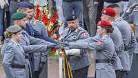 Sechs junge Soldaten legen stehend ihr Hand auf die Truppenfahne, die ein älterer Soldaten hält.