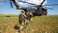 Ein Hubschrauber steht auf einer grünen Wiese und Soldaten laufen auf die Heckklappe zu