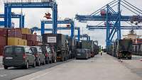 Militärische Fahrzeuge stehen in Reihen im Hafen, im Hintergrund Containerkräne und Container.