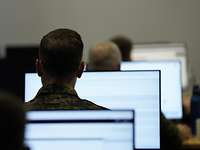 Soldaten sitzen vor hell beleuchteten Computerbildschirmen.