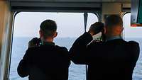 Zwei Soldaten stehen nebeneinander und schauen durch Ferngläser aufs Meer hinaus