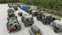 Mehrere Militärfahrzeuge stehen hintereinander in Reihen auf einer Freifläche im Wald