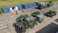 Mehrere Militärfahrzeuge stehen zwischen zwei blauen Containerreihen auf einer Freifläche