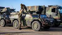 Ein Soldat gibt einem Soldaten, der auf einem Militärfahrzeug steht, eine Holzkiste mit Munition