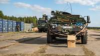 Ein Militärfahrzeug steht hinter einem Papierkarton, auf der linken Seite stehen Container