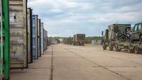 Neben links stehenden Containern fahren mehrere militärische Lkw