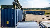 Ein blauer Container wird von einem dafür geeigneten Staplerfahrzeug neben zwei weitere gestellt