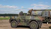 Ein Militärfahrzeug steht neben einem Tankwagen. Ein Mann hockt mit Tankschlauch auf dem Dach