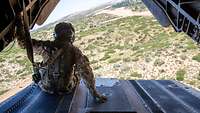 Ein Soldat sitzt auf der Rampe eines fliegenden Hubschraubers.