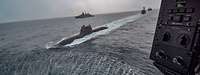 Blick aus einem Hubschrauber auf ein U-Boot und Kriegsschiffe auf hoher See
