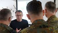 Rückenansicht von drei Soldaten. Sie sprechen mit einem Zivilisten, der vor ihnen steht.