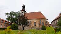 Eine kleine Kirche von außen, links und rechts historische Gebäude.