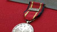 Eine Einsatzmedaille MilEvakOp liegt auf einem roten Stoff.