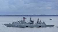 Ein Kriegsschiff und ein gestarteter Hubschrauber auf See