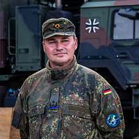 Ein Soldat schaut freundlich ins Gelände, im Hintergrund ein schwerer Lkw