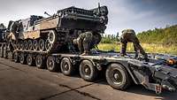 Soldaten verzurren einen Bergepanzer auf einem Schwerlasttransporter.