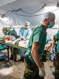 Ein verwundeter Soldat wird auf einer Trage liegend von vier Soldaten aus dem OP der Role 2 getragen
