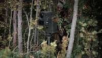 In einem grünen Wald steht ein Soldat an einem grünen Beobachtungsgerät.