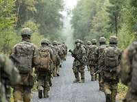 Soldaten mit ABC-Maske und Ausrüstung marschieren in zwei Reihen einen Waldweg entlang