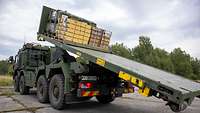 Ein militärischer Lkw hat Kisten auf einer Ladepritsche, die nach hinten gekippt wird .