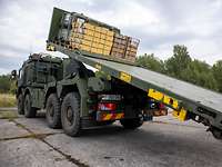 Ein militärischer Lkw hat Kisten auf einer Ladepritsche, die nach hinten gekippt wird .