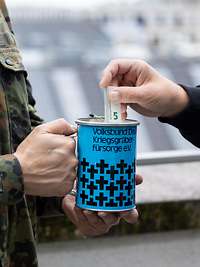 Eine Person steckt Geld in die Sammeldose „Volksbund Deutscher Kriegsgräberfürsorge e.V.“