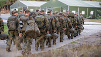 Soldaten mit Ruck- und Schlafsäcken gehen auf ein großes Zelt zu