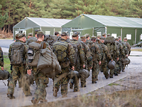 Soldaten mit Ruck- und Schlafsäcken gehen auf ein großes Zelt zu