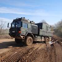 Ein Transportfahrzeug der Bundeswehr fährt, schräg zum Betrachter auf, offenem Gelände.