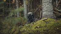 Soldat liegt mit Sturmgewehr im Wald und beobachtet das Gelände.