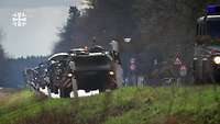 Fahrzeuge der Bundeswehr fahren auf einer Landstraße auf den Betrachter zu.