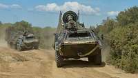 Zwei Radpanzer fahren in sandigem Gelände.