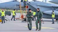 Ein japanischer und ein deutscher Soldat reichen sich die Hände, im Hintergrund sieht man eine F-15.