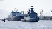 Ein graues Marineschiff und ein Fähre laufen aus dem Rostocker Hafen aus.